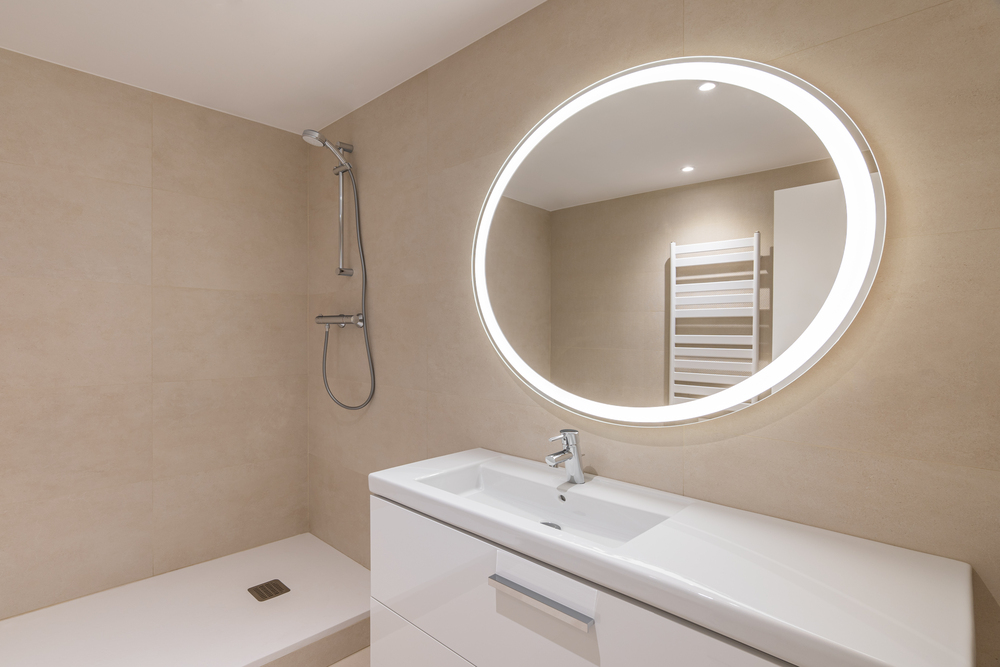 Baño elegante con espejo LED iluminado, ideal para mejorar la visibilidad y funcionalidad, complementado con una ducha minimalista y toallero integrado.